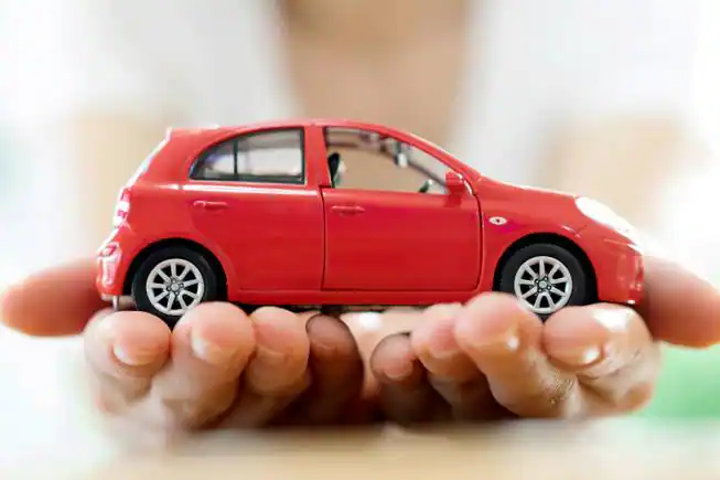 Car refinance concept image: Red toy car held in cupped hands, representing lower car payments